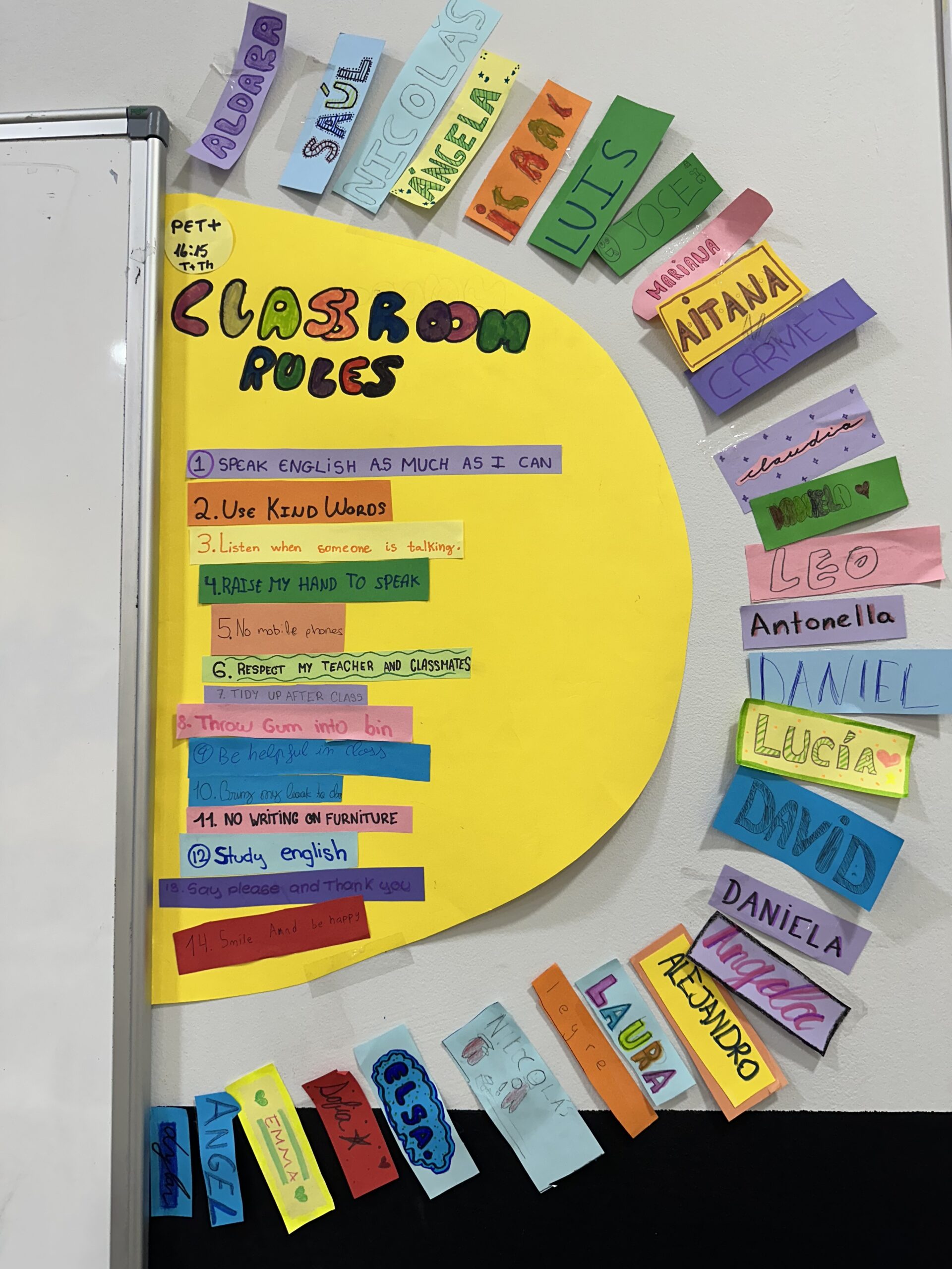 Decoración de medio sol junto a la pizarra en la academia Royal English Valdemoro, con normas escritas en el centro y rayos formados por los nombres de los alumnos.
