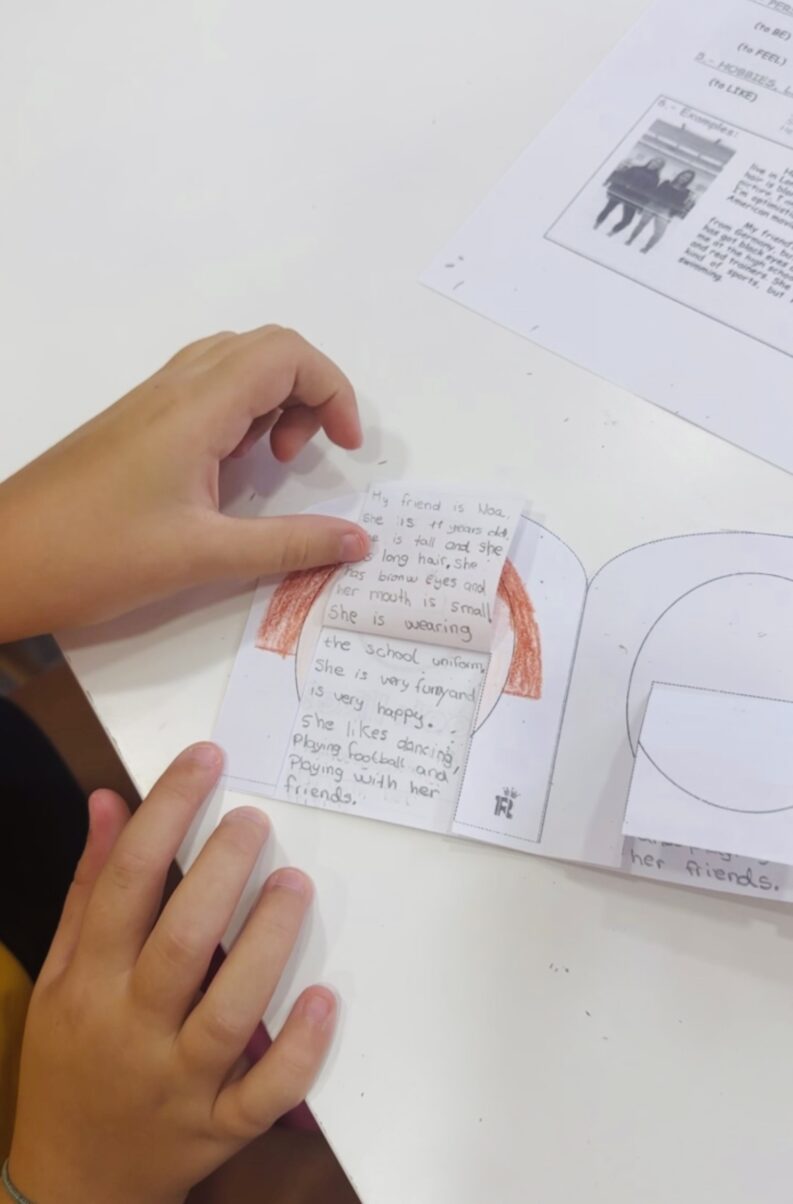 Un alumno de la academia Royal English Valdemoro muestra con sus manos un librito artesanal en inglés, donde describe a personas importantes para él con dibujos y vocabulario descriptivo.